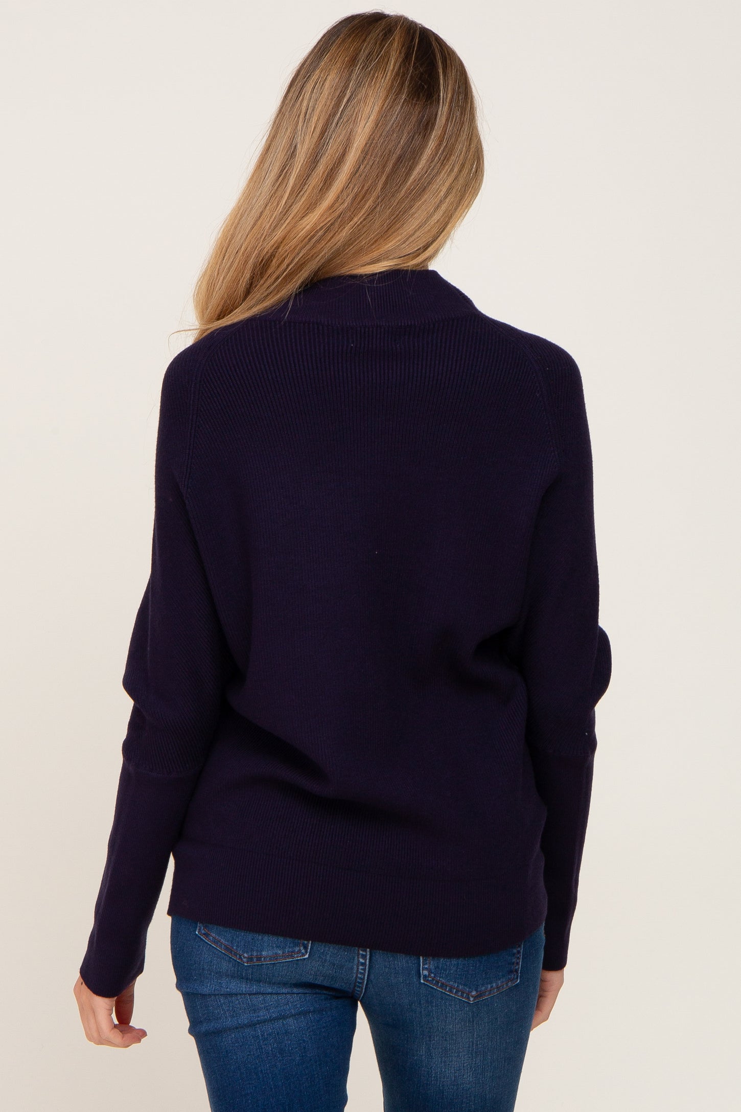 back view of a woman with blonde hair wearing a navy blue ribbed knit sweater and blue jeans