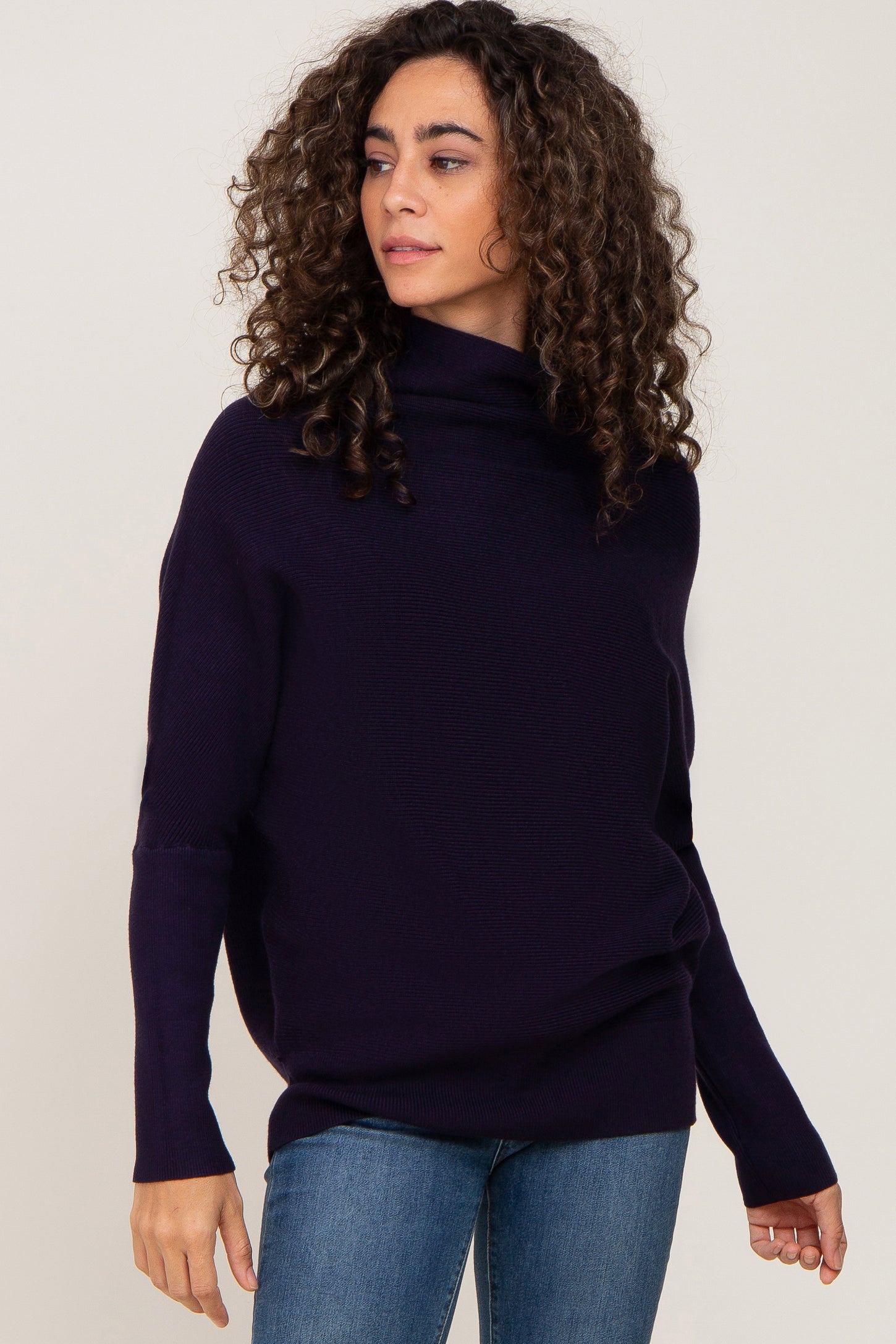 woman with curly hair wearing a navy blue ribbed turtleneck sweater and blue jeans