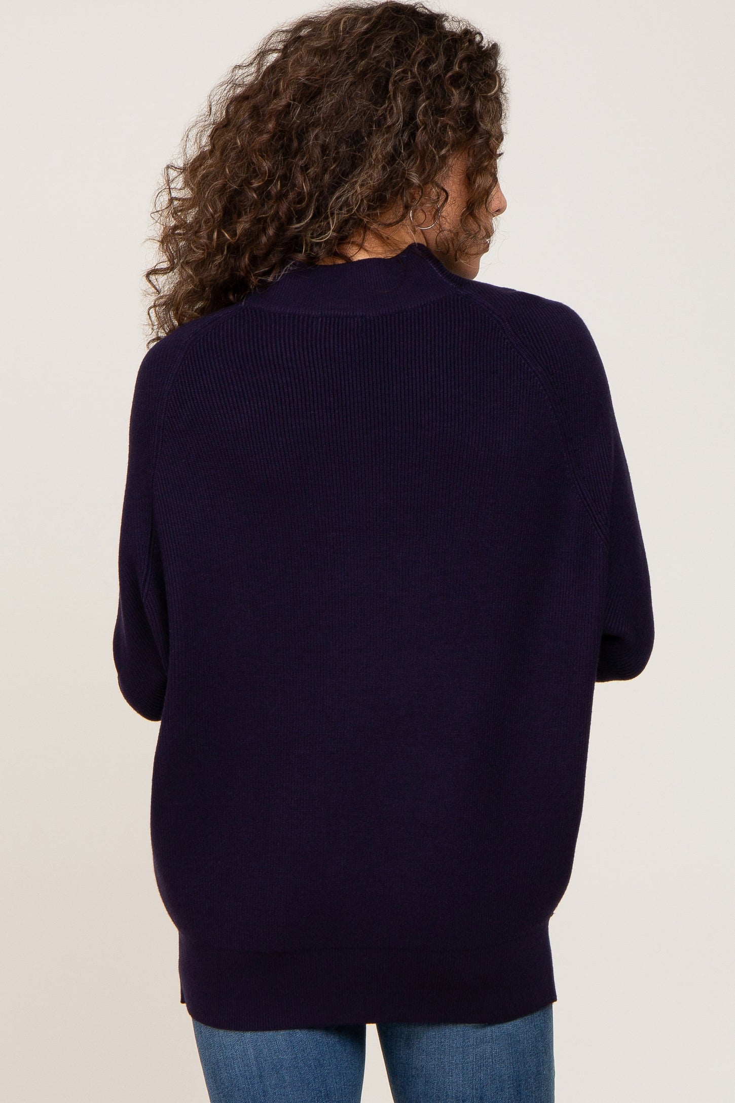 Back view of a woman with curly hair wearing a dark navy blue ribbed knit sweater and blue jeans