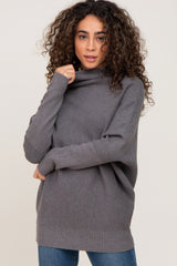 woman with curly hair wearing a grey oversized turtleneck sweater and blue jeans