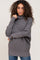 woman with curly hair wearing a grey oversized turtleneck sweater and blue jeans
