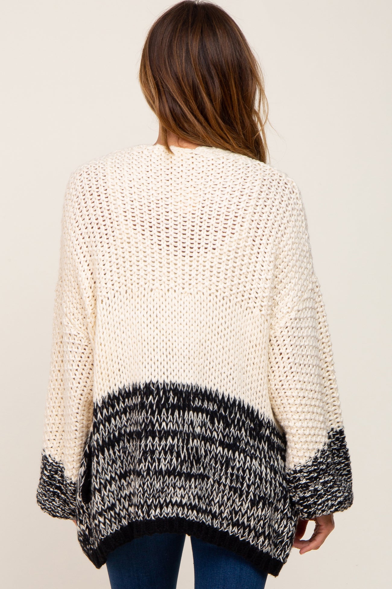 Back view of a woman wearing a cream and black colorblock chunky knit cardigan sweater