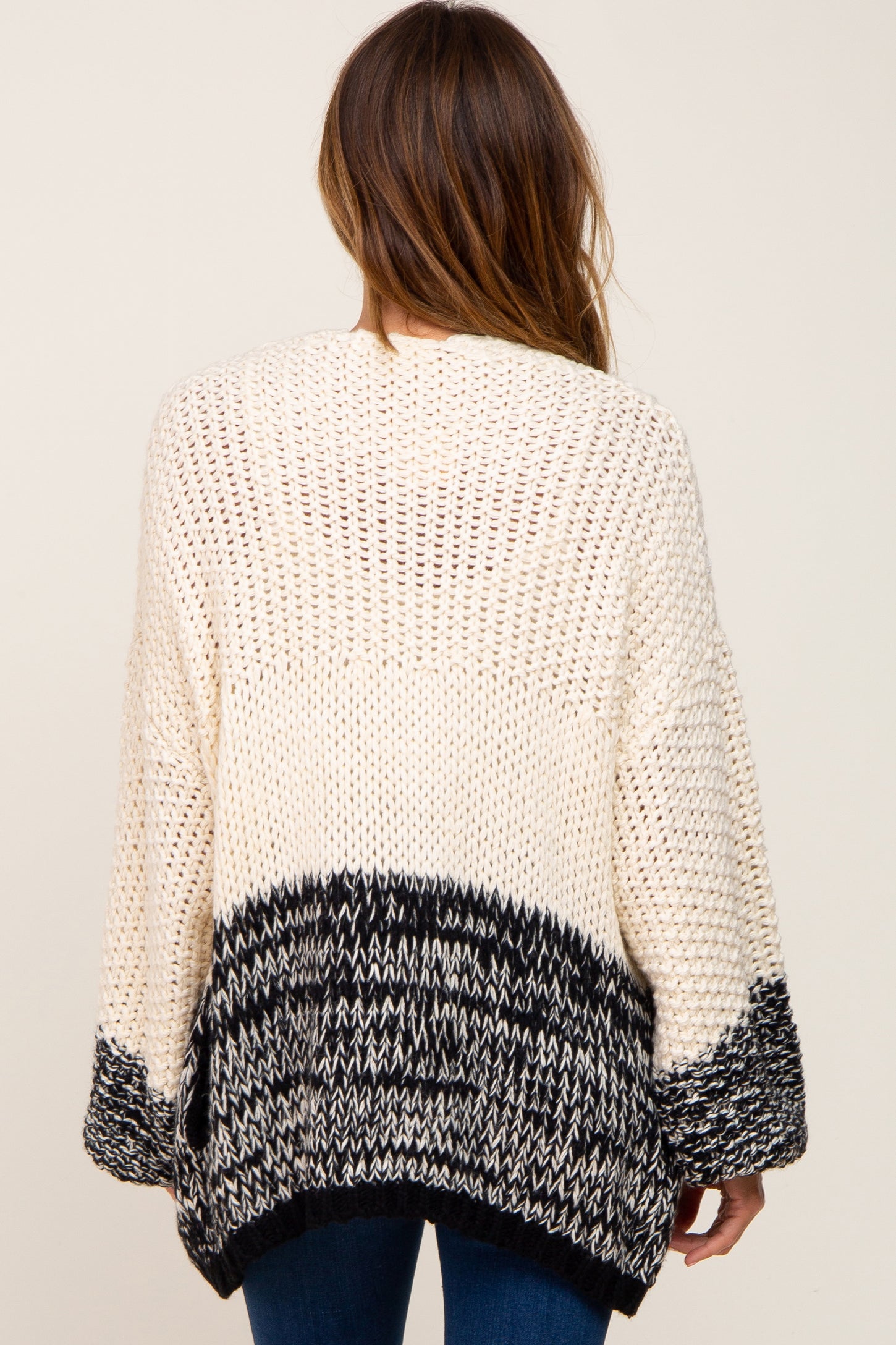 Back view of a woman wearing a cream and black colorblock chunky knit cardigan sweater