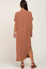 back view of a woman wearing a short sleeve rust colored maxi shirt dress with side slits and brown sandals
