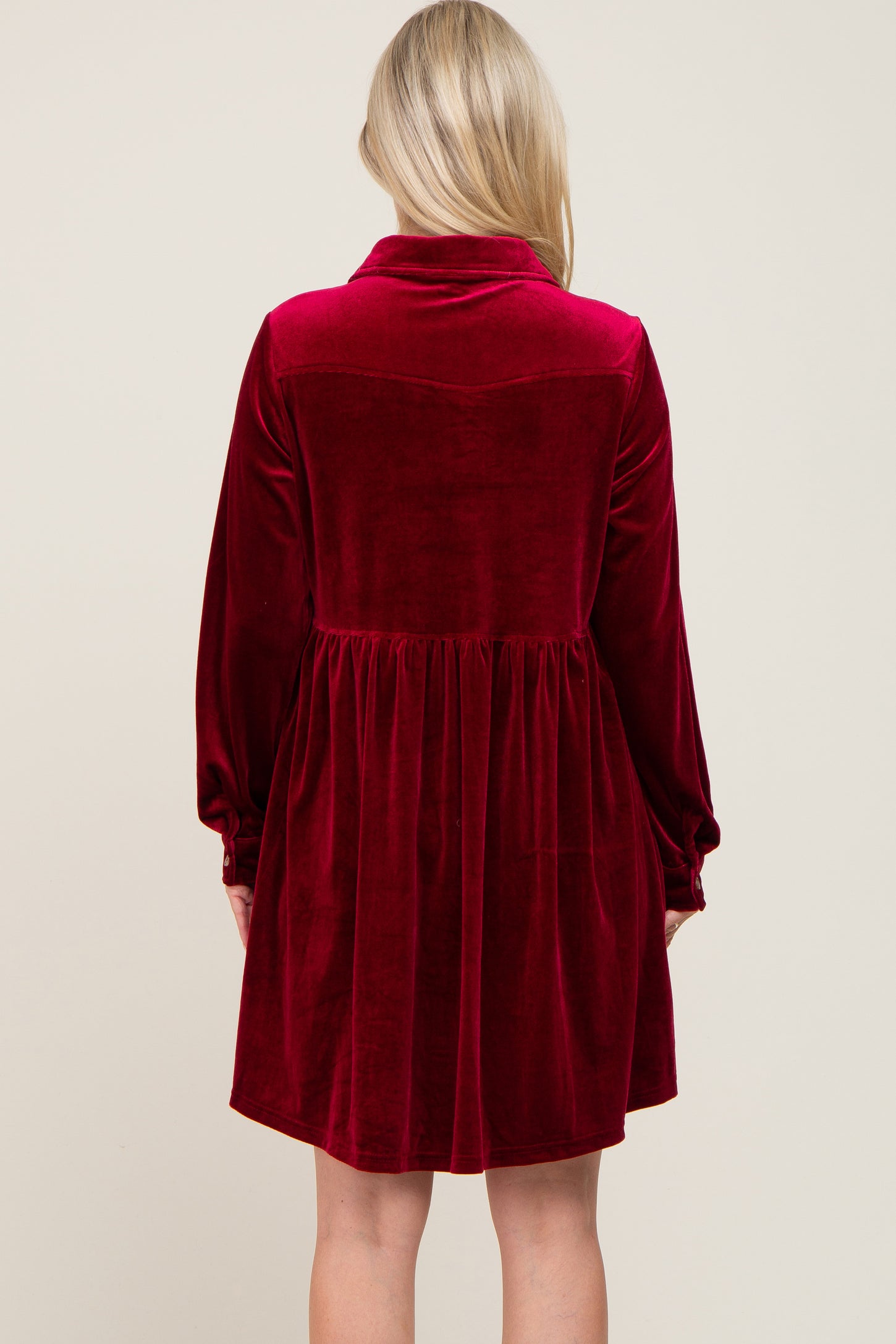 back view of a woman wearing a long sleeve burgundy velvet babydoll dress with a collared neckline