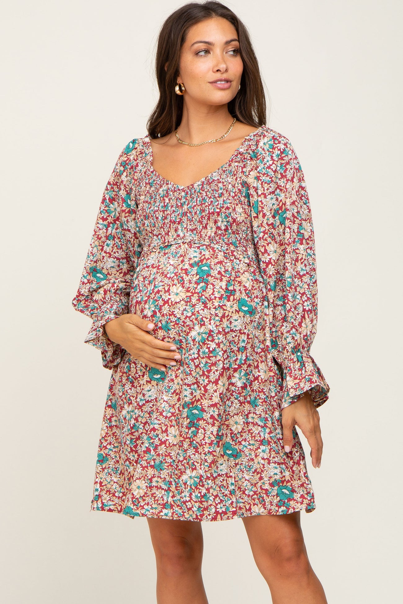 pregnant woman wearing a floral smocked maternity mini dress with long sleeves and gold jewelry