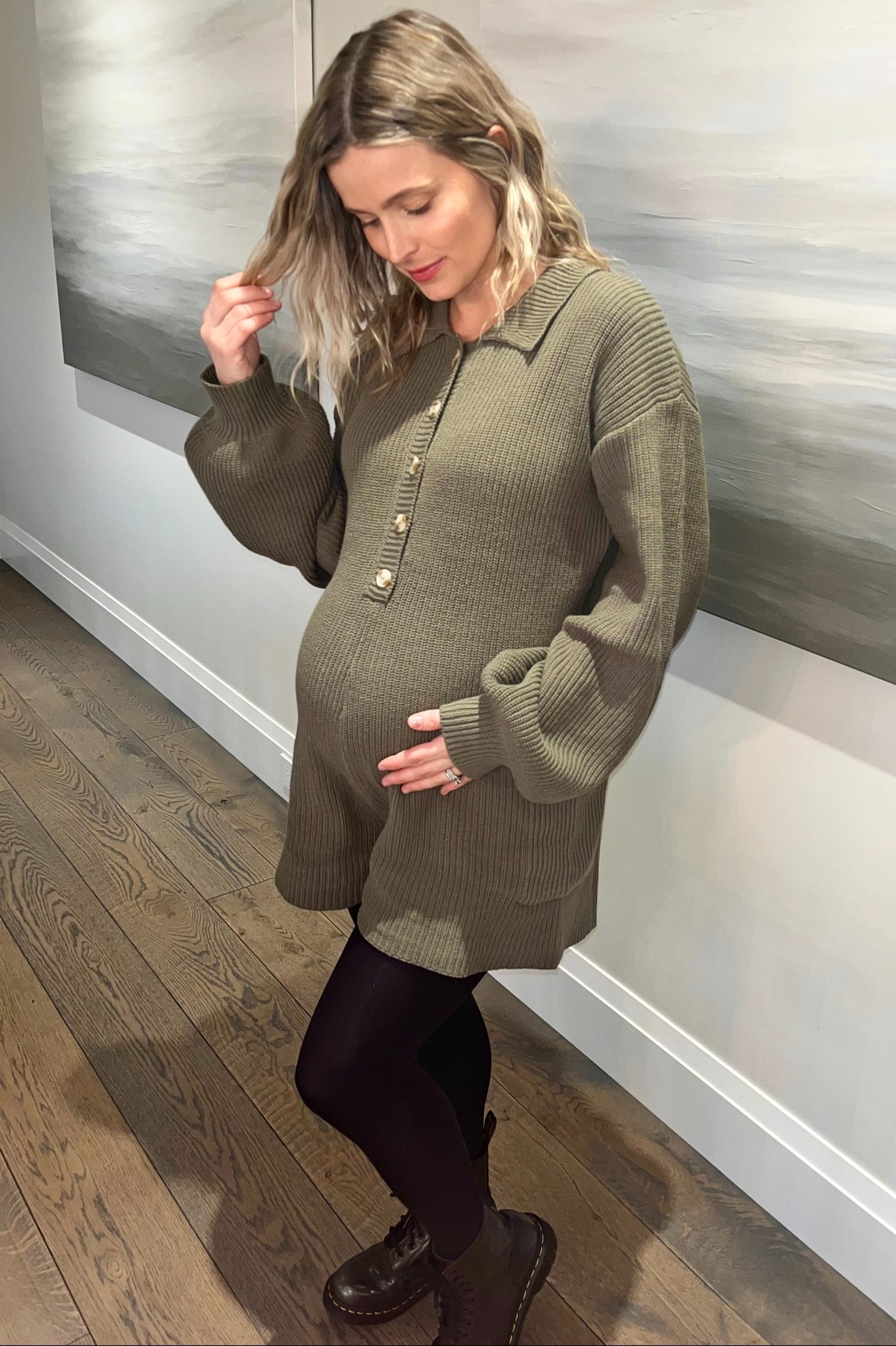 pregnant woman wearing olive green ribbed knit maternity dress and black leggings standing on hardwood floor