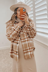 woman wearing a tan plaid shacket and wide brim hat taking a mirror selfie with an orange phone case