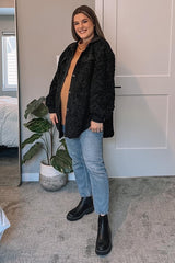 woman wearing black sherpa jacket, tan sweater, blue jeans, and black chelsea boots in a bedroom