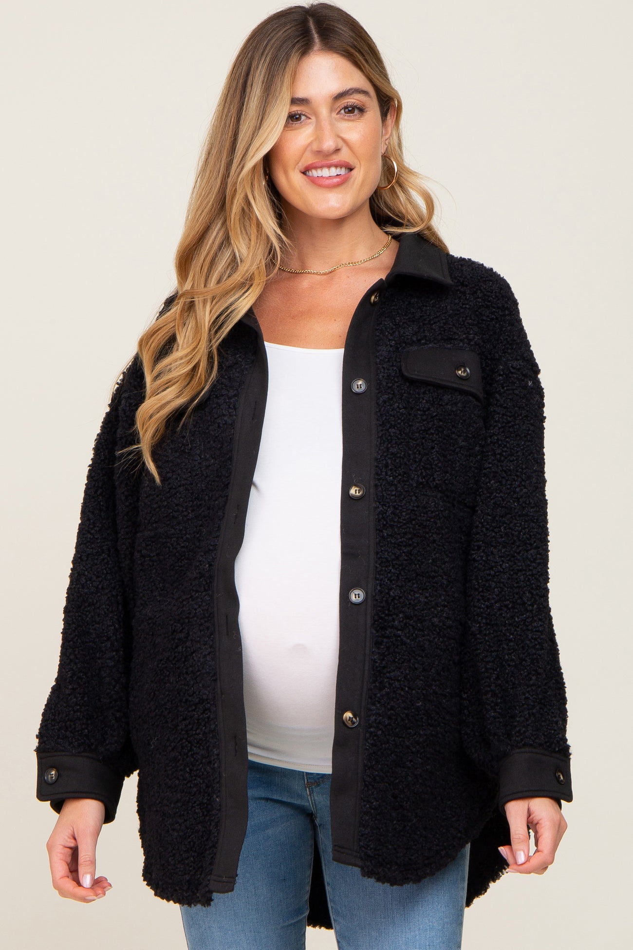 Pregnant woman wearing a black sherpa maternity shacket over a white top and blue jeans