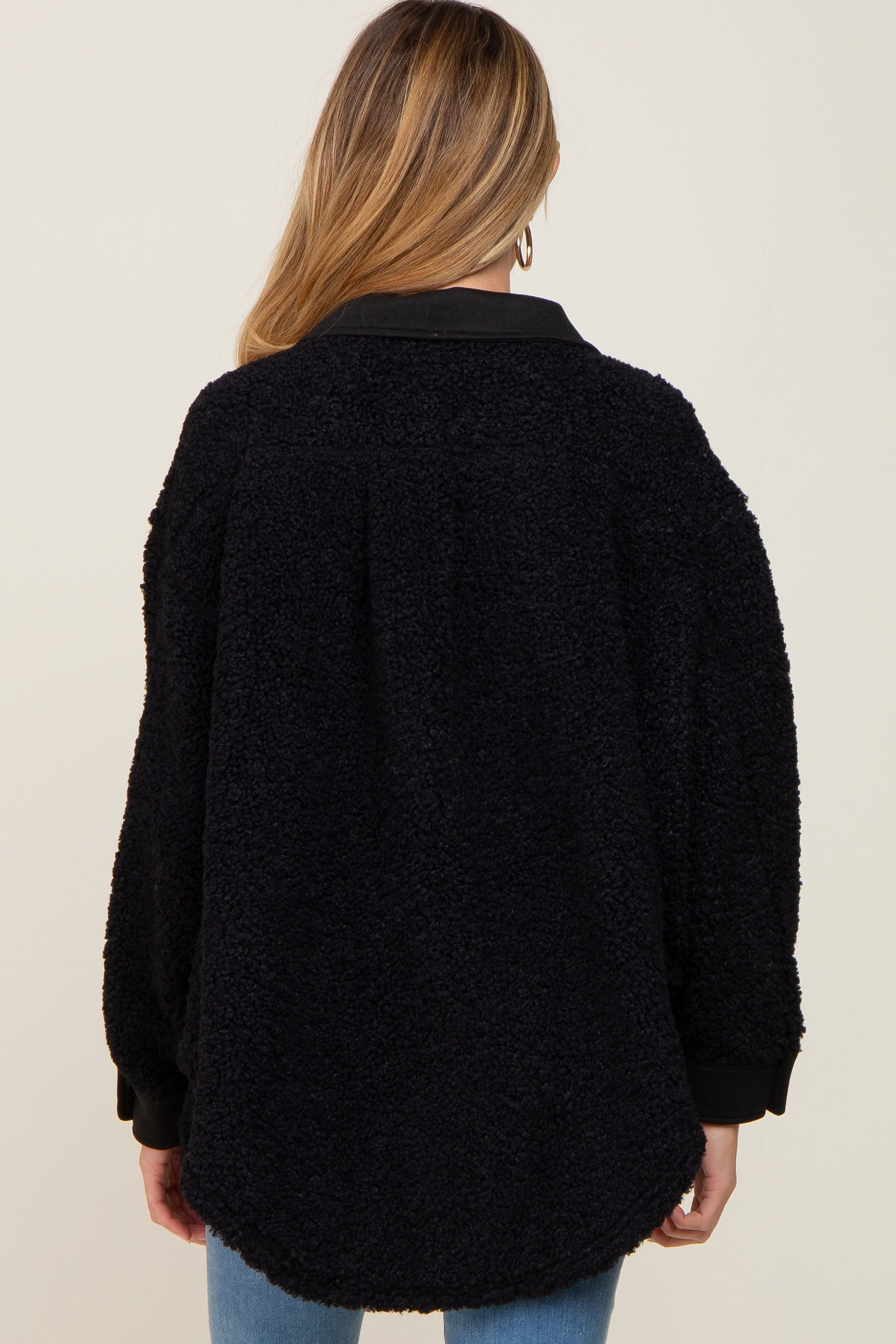 Back view of a woman wearing a black oversized sherpa fleece jacket with a collar and ribbed cuffs