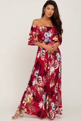 Woman wearing a red off-the-shoulder floral maxi dress with tropical leaf print and white sandals