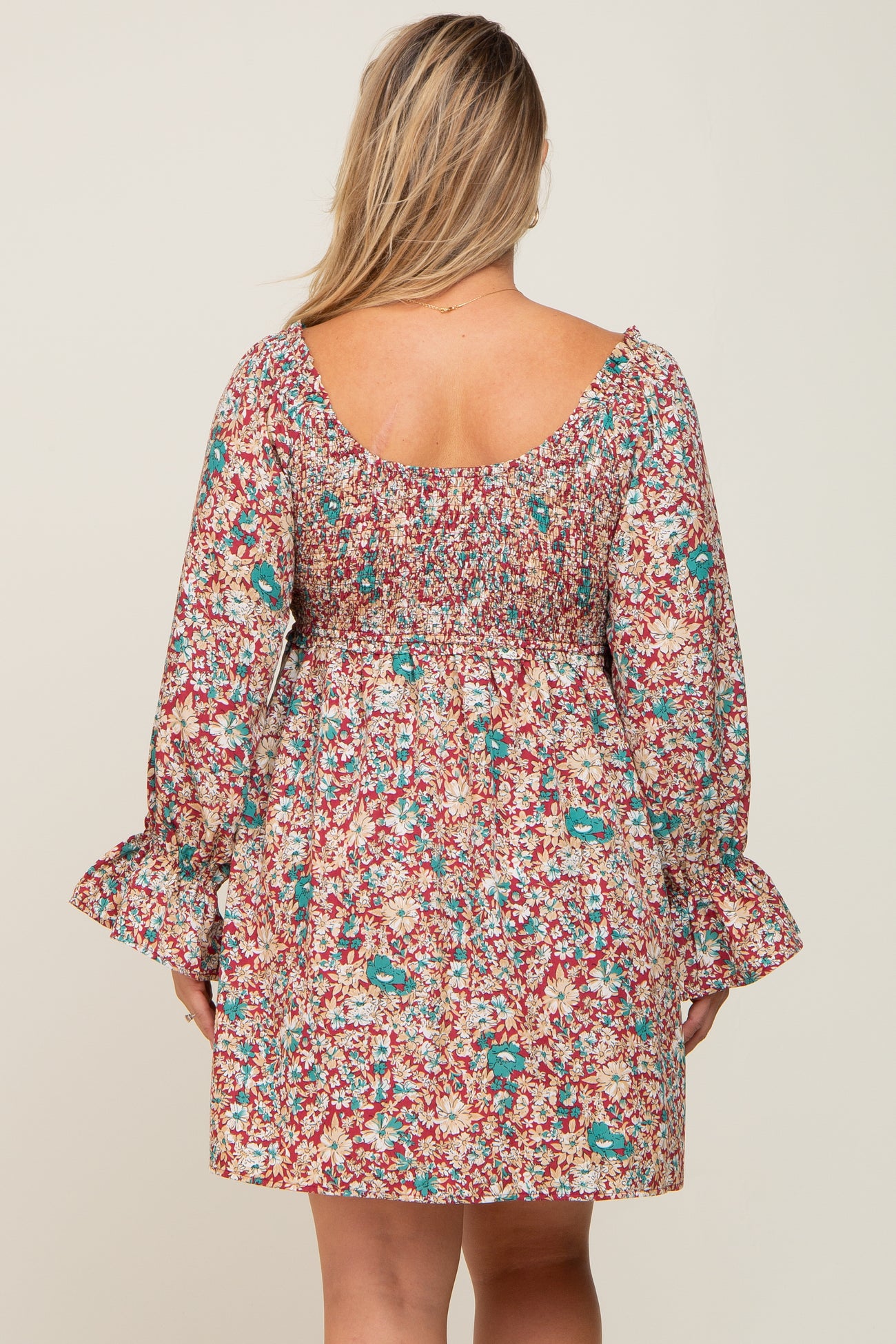 Back view of a woman wearing a red floral smocked mini dress with long bell sleeves and a square neckline