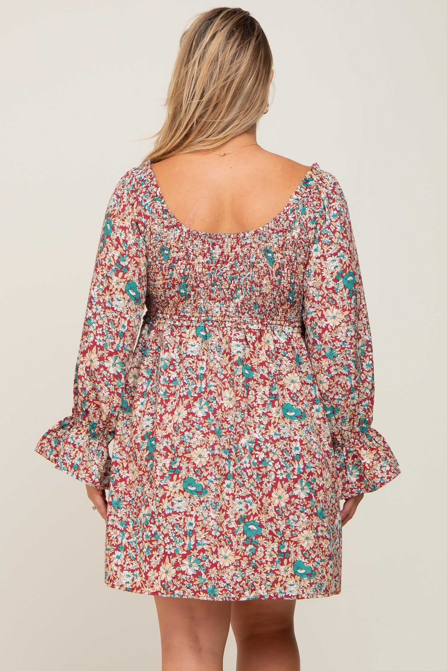 Back view of a woman wearing a red floral smocked mini dress with long bell sleeves and a square neckline