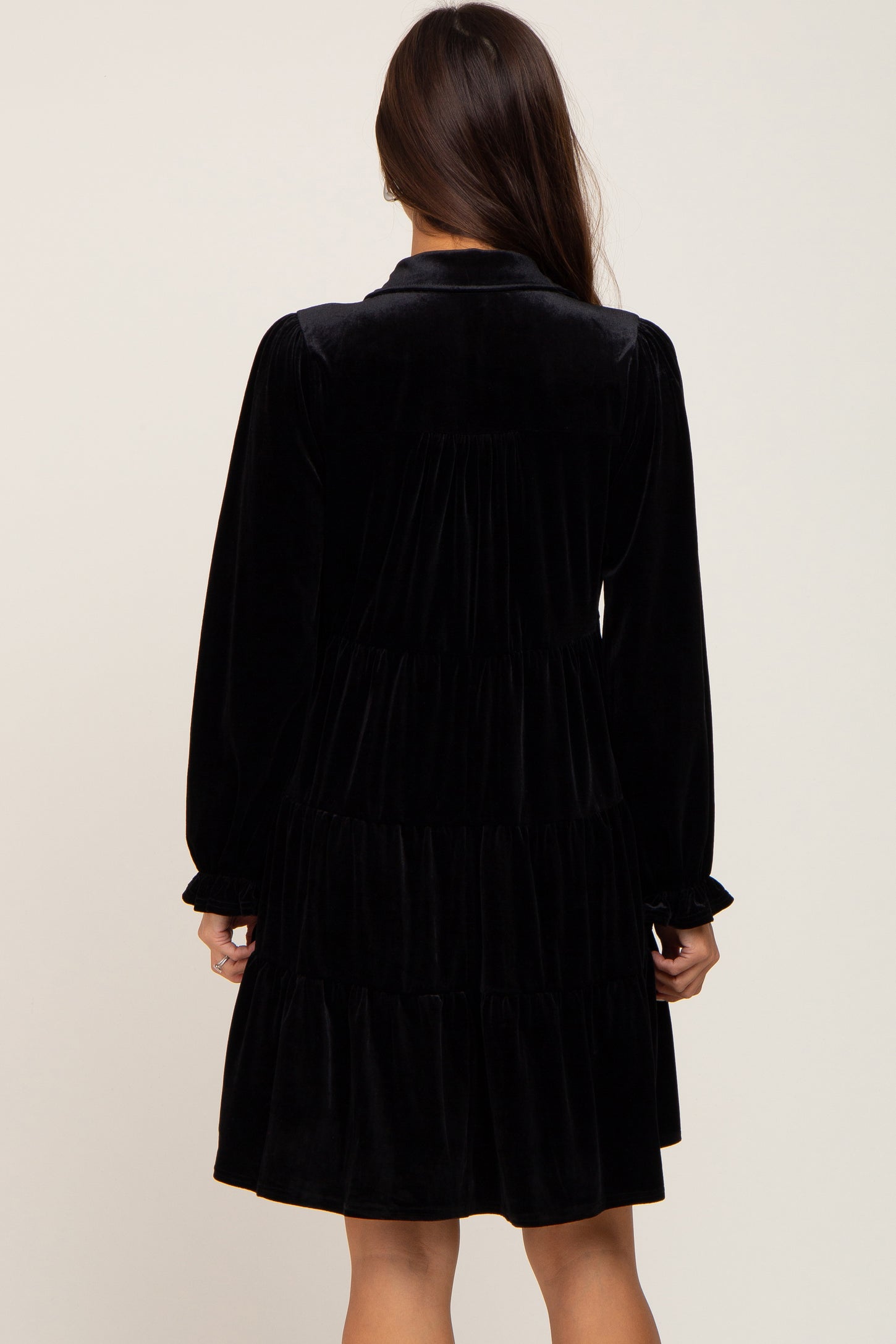 Back view of a woman wearing a black long-sleeve tiered velvet mini dress with a collar