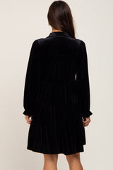 Back view of a woman wearing a black long-sleeve tiered velvet mini dress with a collar