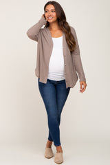 woman wearing a tan ribbed maternity cardigan over a white top and blue maternity jeans, smiling and holding her baby bump