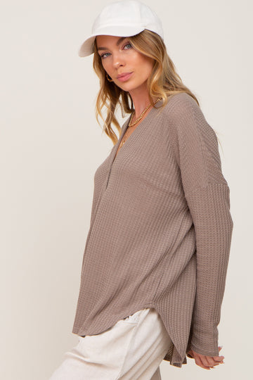 woman wearing a light taupe long sleeve top with a v-neck and side slits, paired with a white cap