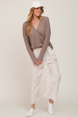 woman wearing a taupe button-up ribbed cardigan, cream pants, and a white cap, styled casually with white sneakers