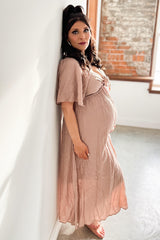 woman wearing a blush pink maternity dress with short flutter sleeves, standing and showing her baby bump