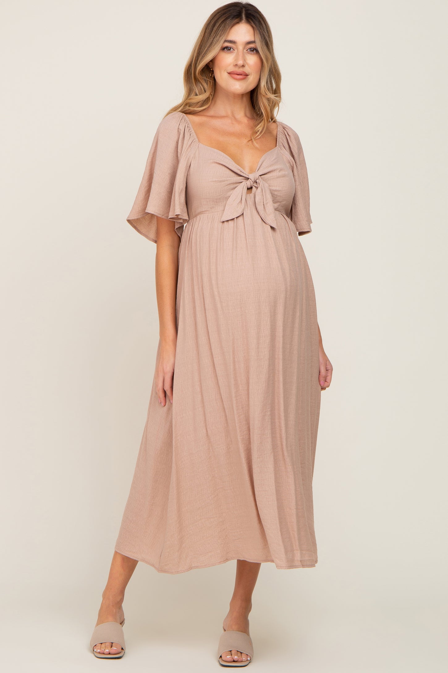 woman wearing a blush pink maternity dress with a tie front detail and flowing sleeves, highlighting her baby bump