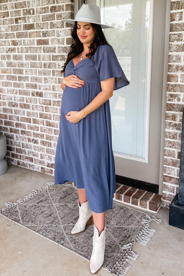 woman wearing a navy blue maternity maxi dress with flutter sleeves and holding her baby bump, standing outdoors