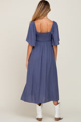 woman wearing a navy blue maternity maxi dress with puff sleeves and a smocked bodice, showing her back