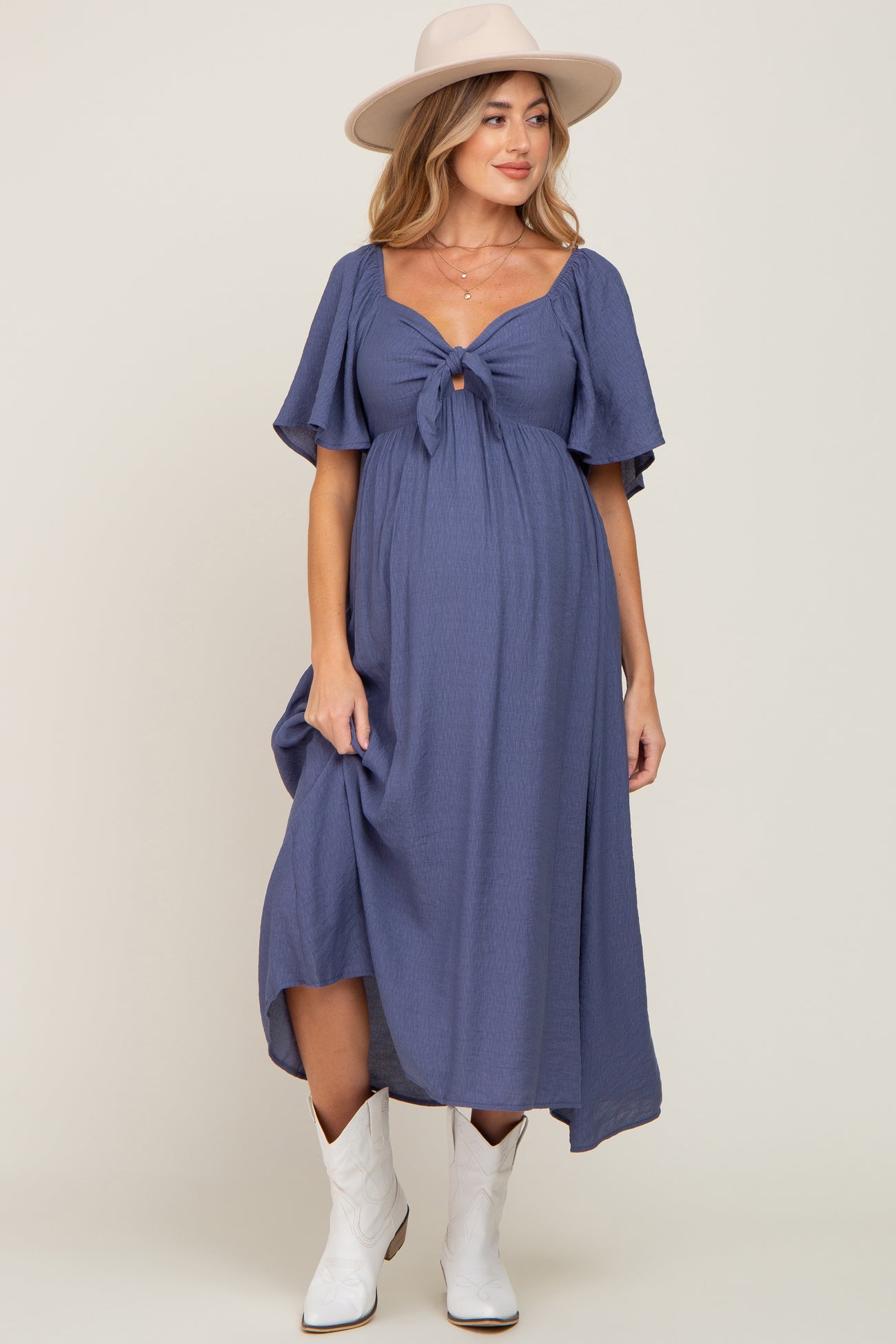 woman wearing a dusty blue maternity dress with short flutter sleeves and a front tie, showing her baby bump