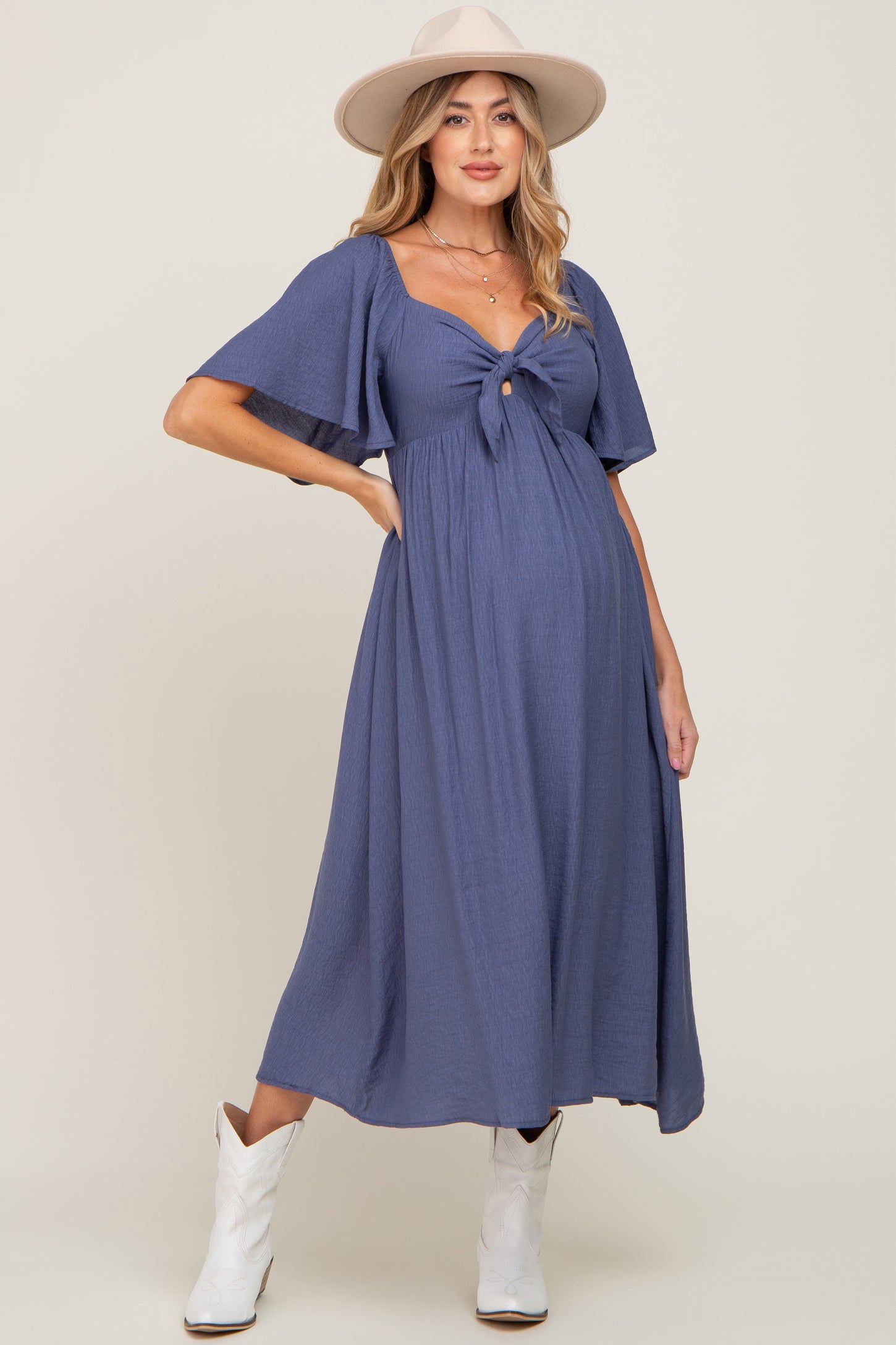 woman wearing a navy blue maternity dress with short flutter sleeves and a front knot, highlighting her baby bump