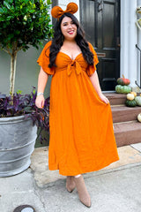 woman wearing an orange maxi dress with flutter sleeves and a tie front, accessorized with mouse ears headband