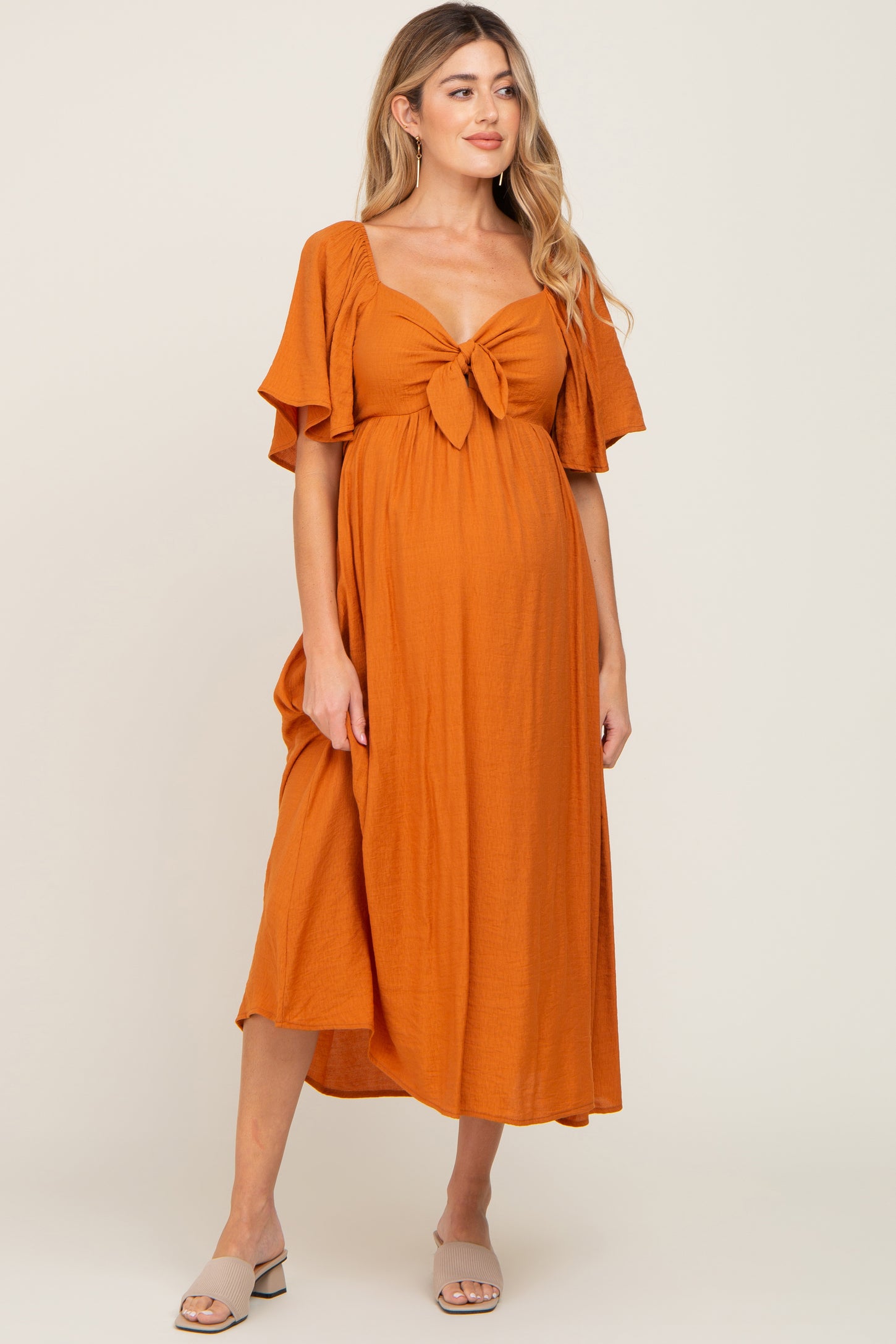 woman wearing an orange maternity dress with a tied front and flutter sleeves, showcasing her baby bump