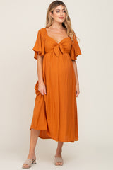 woman wearing an orange maternity dress with a tied front and flutter sleeves, showcasing her baby bump