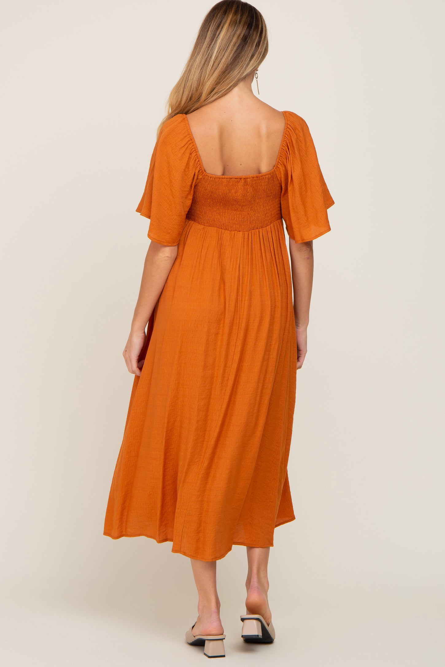 woman wearing an orange maternity dress with a smocked bodice and flutter sleeves, standing with her back to the camera
