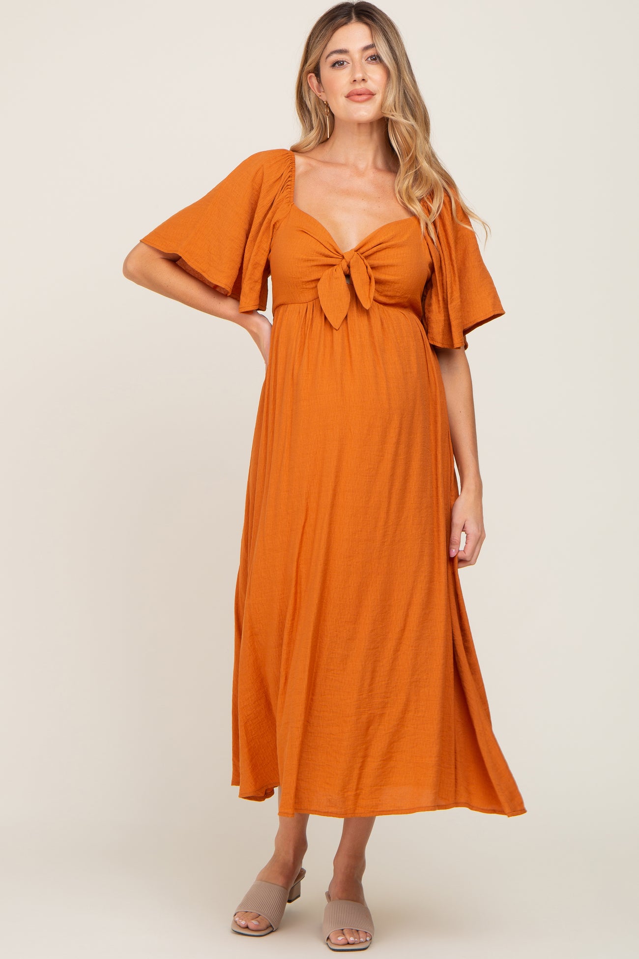 woman wearing an orange maternity maxi dress with short sleeves and a knot detail at the bust, showing her baby bump