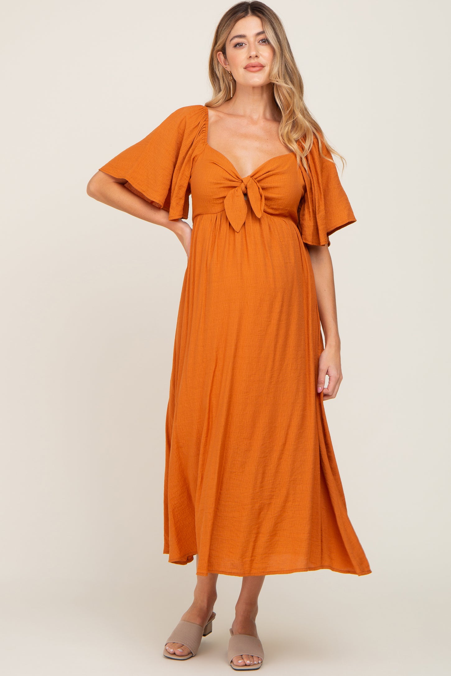 woman wearing an orange maternity maxi dress with short sleeves and a knot detail at the bust, showing her baby bump