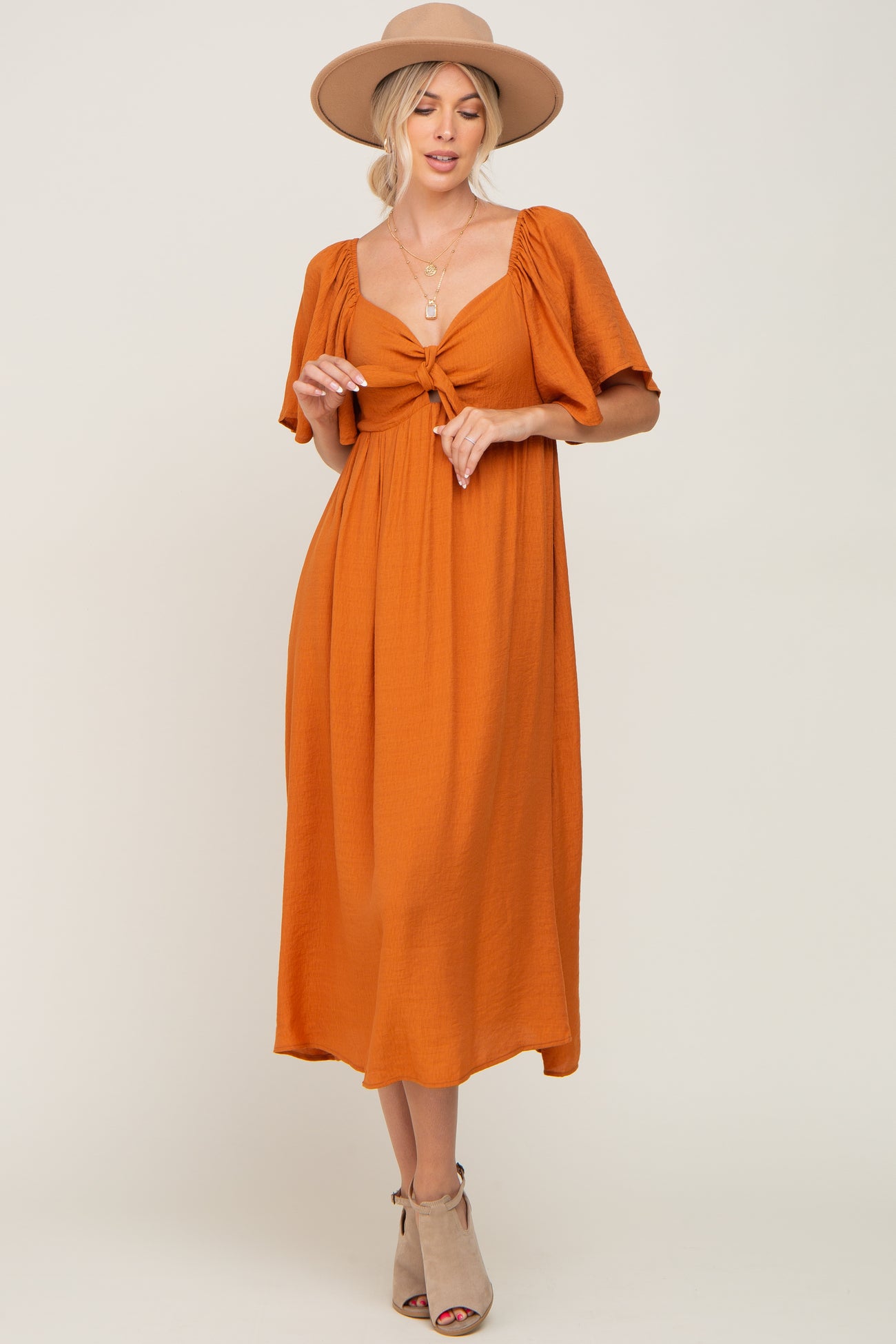 woman wearing an orange midi dress with puff sleeves and a knotted front, paired with a wide-brim hat and ankle boots