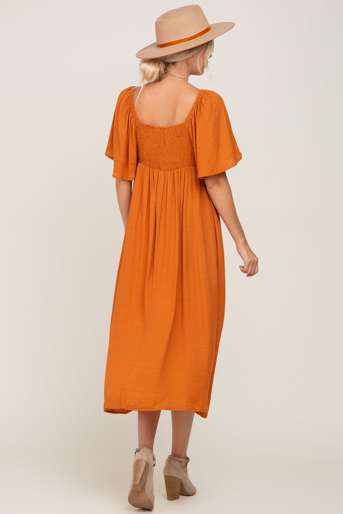 woman wearing an orange midi dress with short sleeves and a smocked back, styled with a beige hat