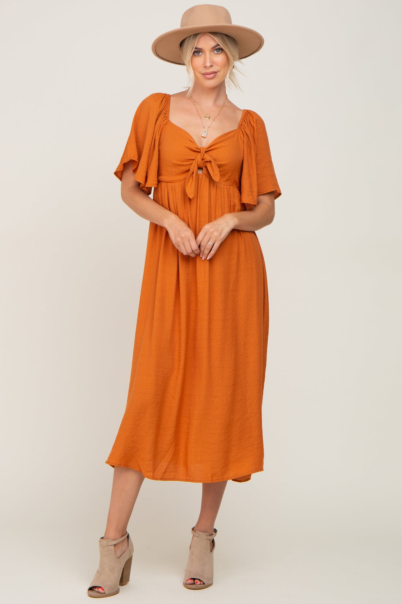 woman wearing an orange midi dress with short sleeves and a tie front, paired with a wide-brim hat and heeled sandals