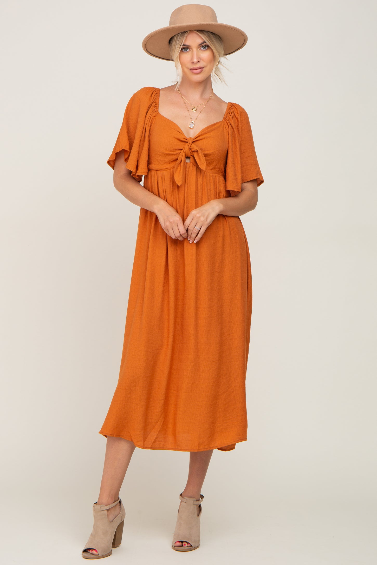 woman wearing an orange midi dress with short sleeves and a tie front, paired with a wide-brim hat and heeled sandals