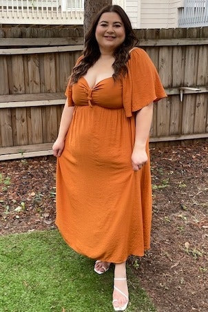 woman wearing an orange maxi dress with a knotted front detail and flutter sleeves, standing in a backyard