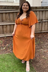 woman wearing an orange maxi dress with a knotted front detail and flutter sleeves, standing in a backyard
