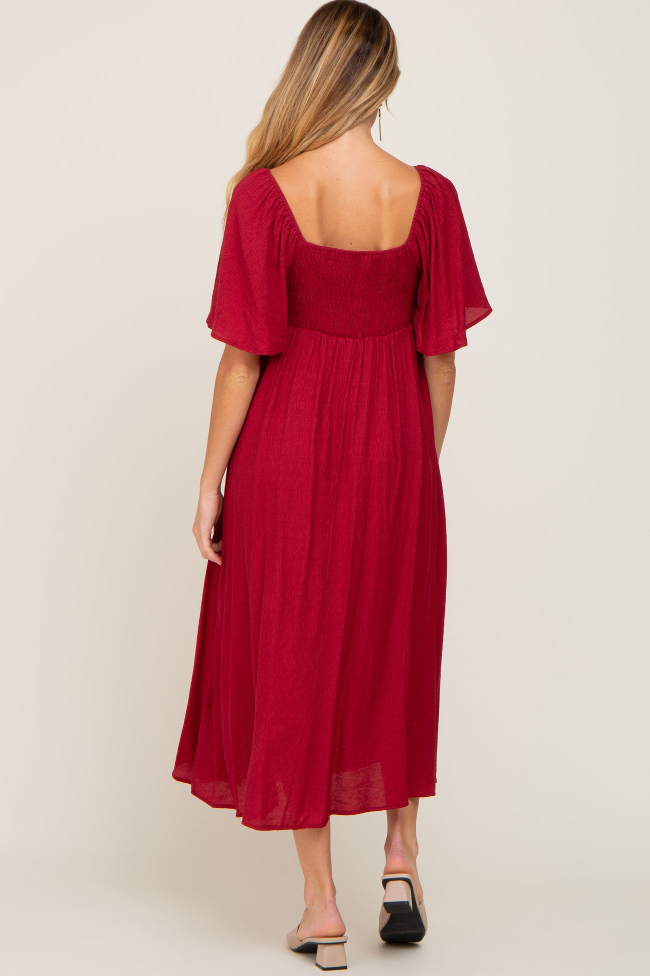 woman wearing a red maternity dress with short flutter sleeves and a flowy skirt, showing the back view