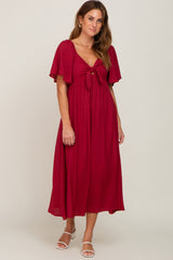 woman wearing a burgundy flutter sleeve midi dress with a front tie detail and white sandals