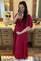 woman wearing a red maternity maxi dress with a bow detail, holding her baby bump in a bathroom mirror selfie