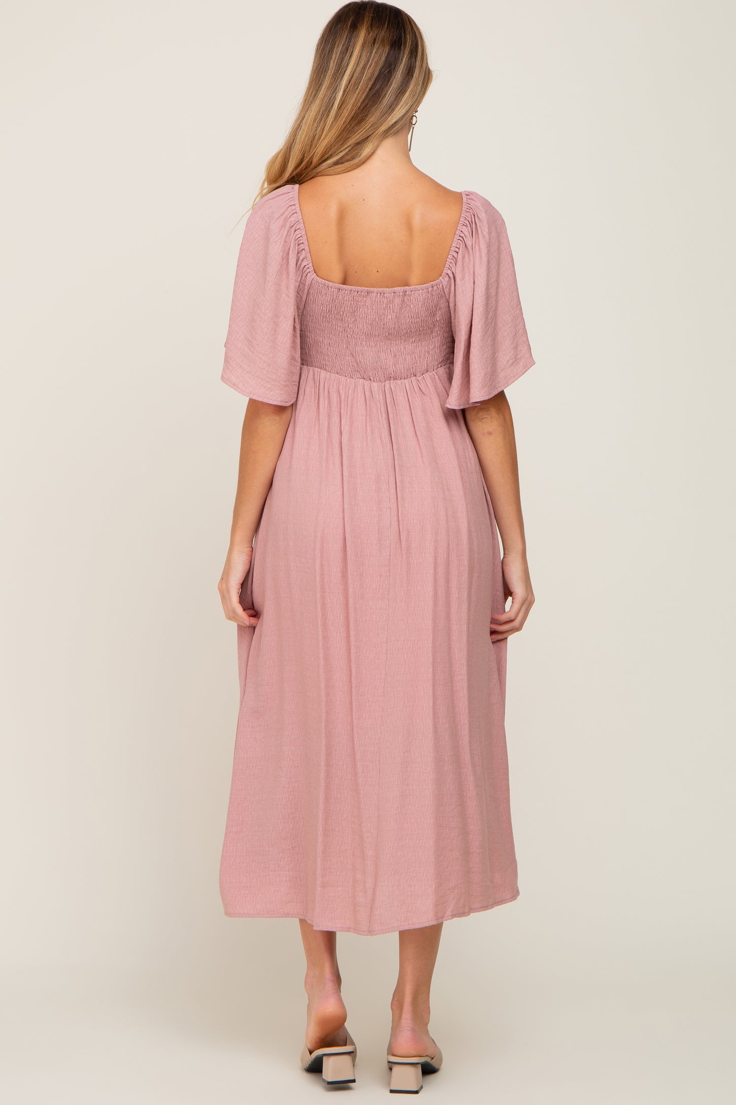 woman wearing a pink maternity dress with short sleeves and a smocked bodice, showing the back view
