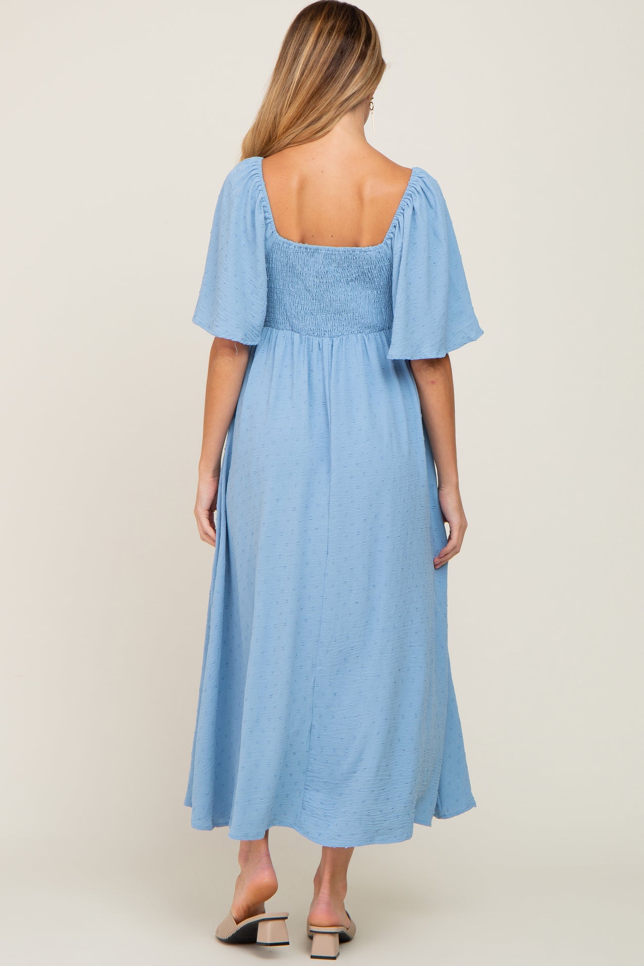 woman wearing a light blue maternity midi dress with short puff sleeves and smocked bodice, showing a baby bump from behind
