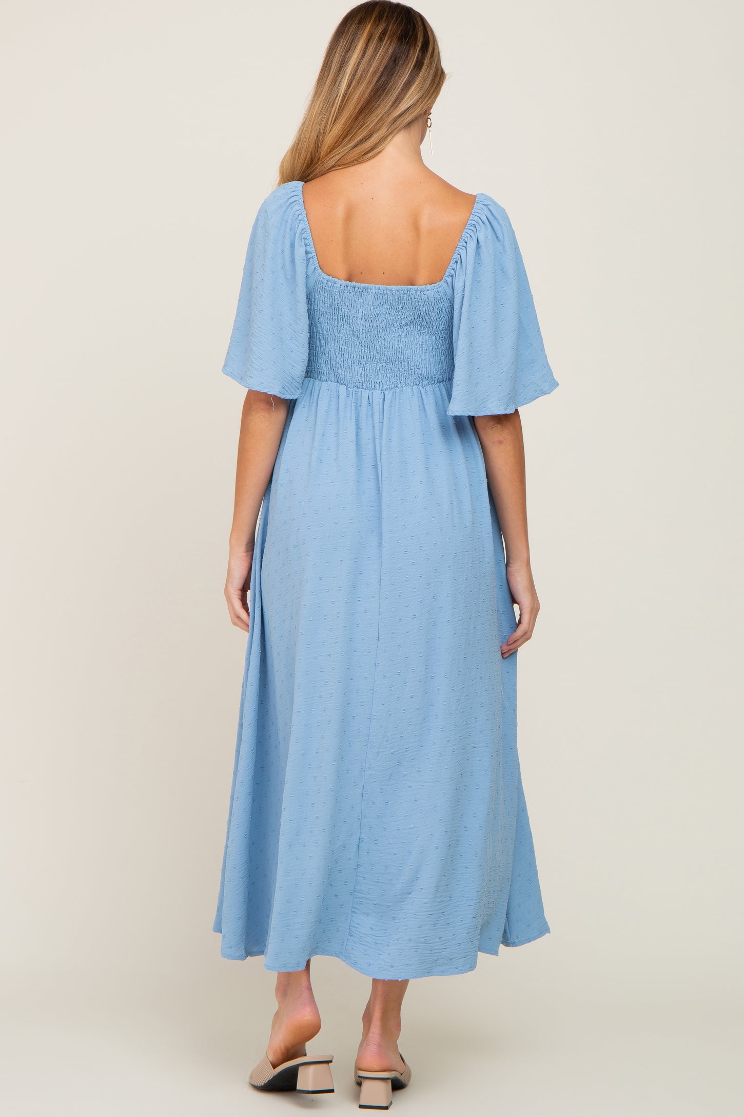 woman wearing a light blue maternity midi dress with short puff sleeves and smocked bodice, showing a baby bump from behind