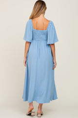 woman wearing a light blue maternity midi dress with short puff sleeves and smocked bodice, showing a baby bump from behind