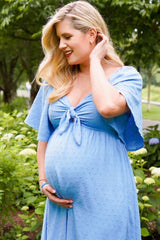 woman wearing a light blue maternity dress with a tie front detail and baby bump in a floral outdoor setting