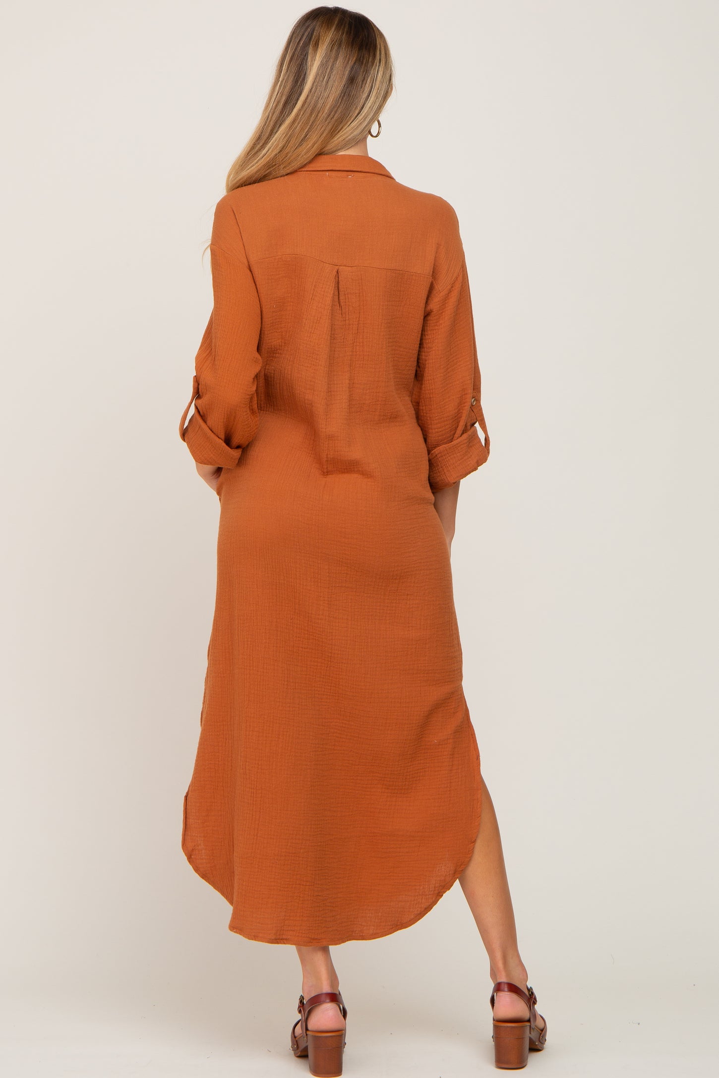 back view of woman wearing rust orange long sleeve gauze shirt dress with high low hem and brown sandals